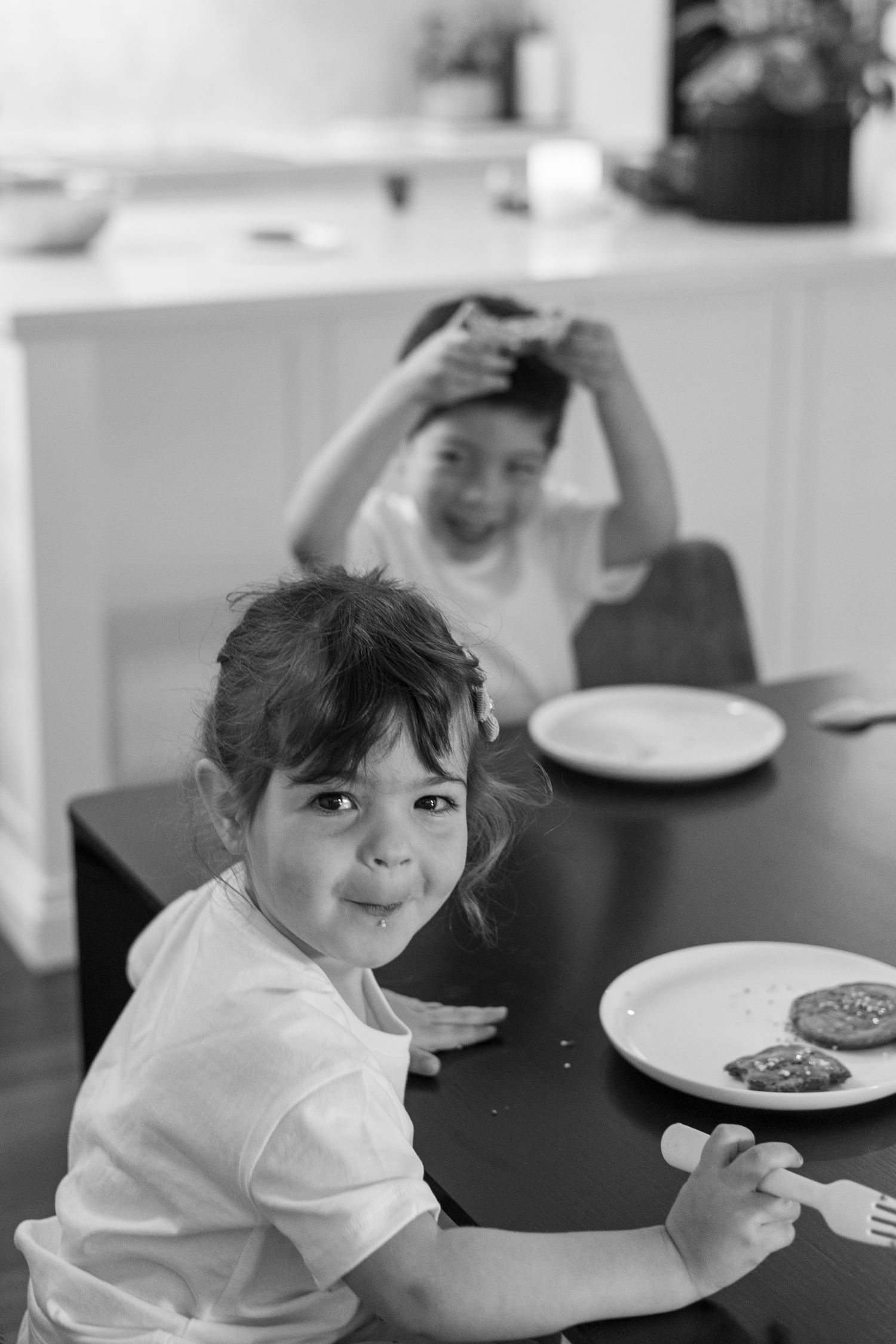 Black and white photo of children enjoying cookies at a dining table in a kitchen setting.
