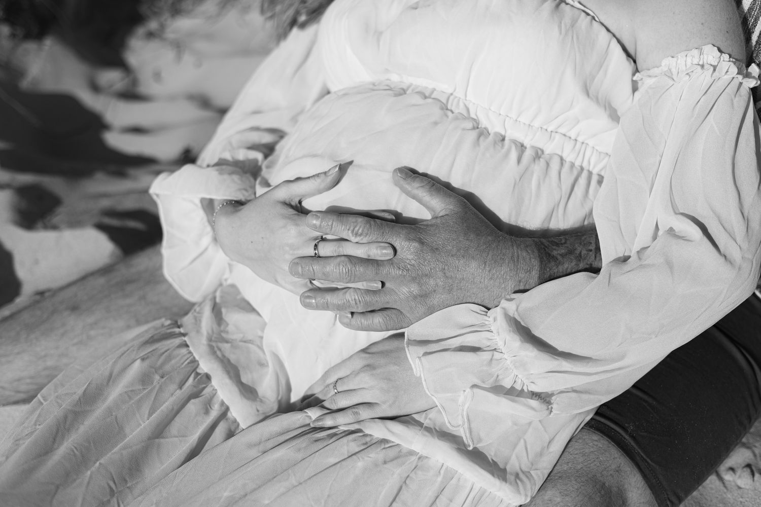 Black and white close-up of hands resting on a ruffled white dress or fabric.
