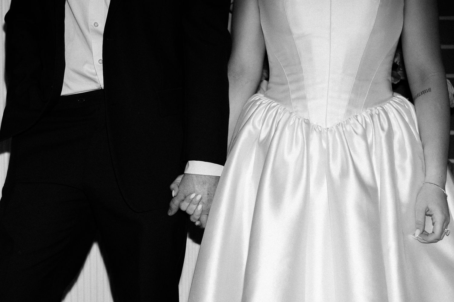 A row of wedding party members wearing black suits and white dresses stand against a dark background.