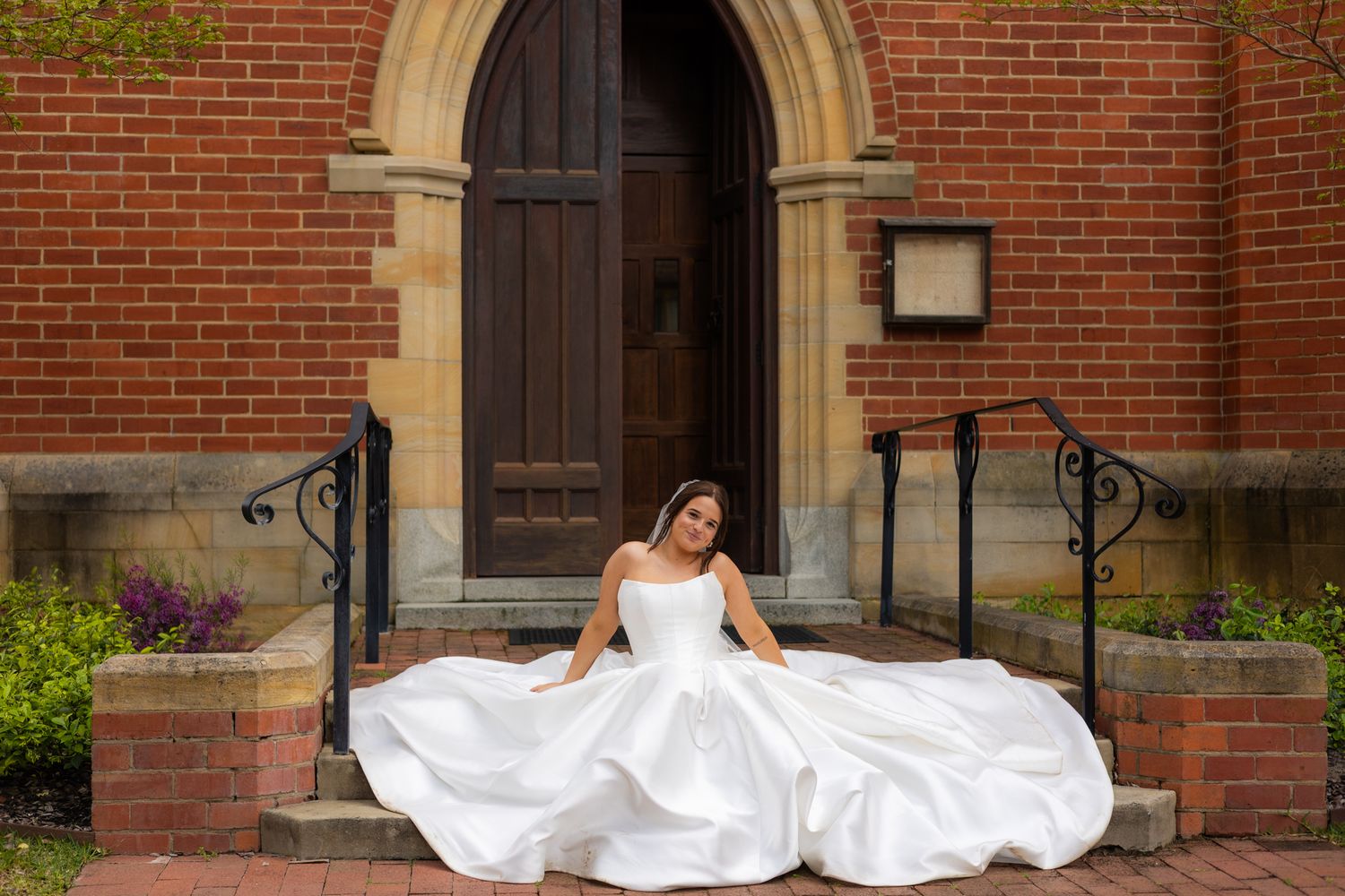 A bride in a flowing white gown poses elegantly on brick steps in front of an arched doorway. Perth wedding documentary photography, elopeme