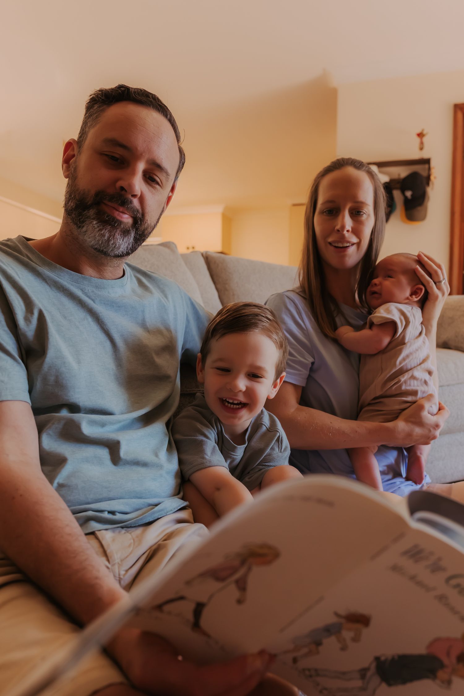 A parent and child share a cozy moment reading a book together on a bed in a warm-toned room.