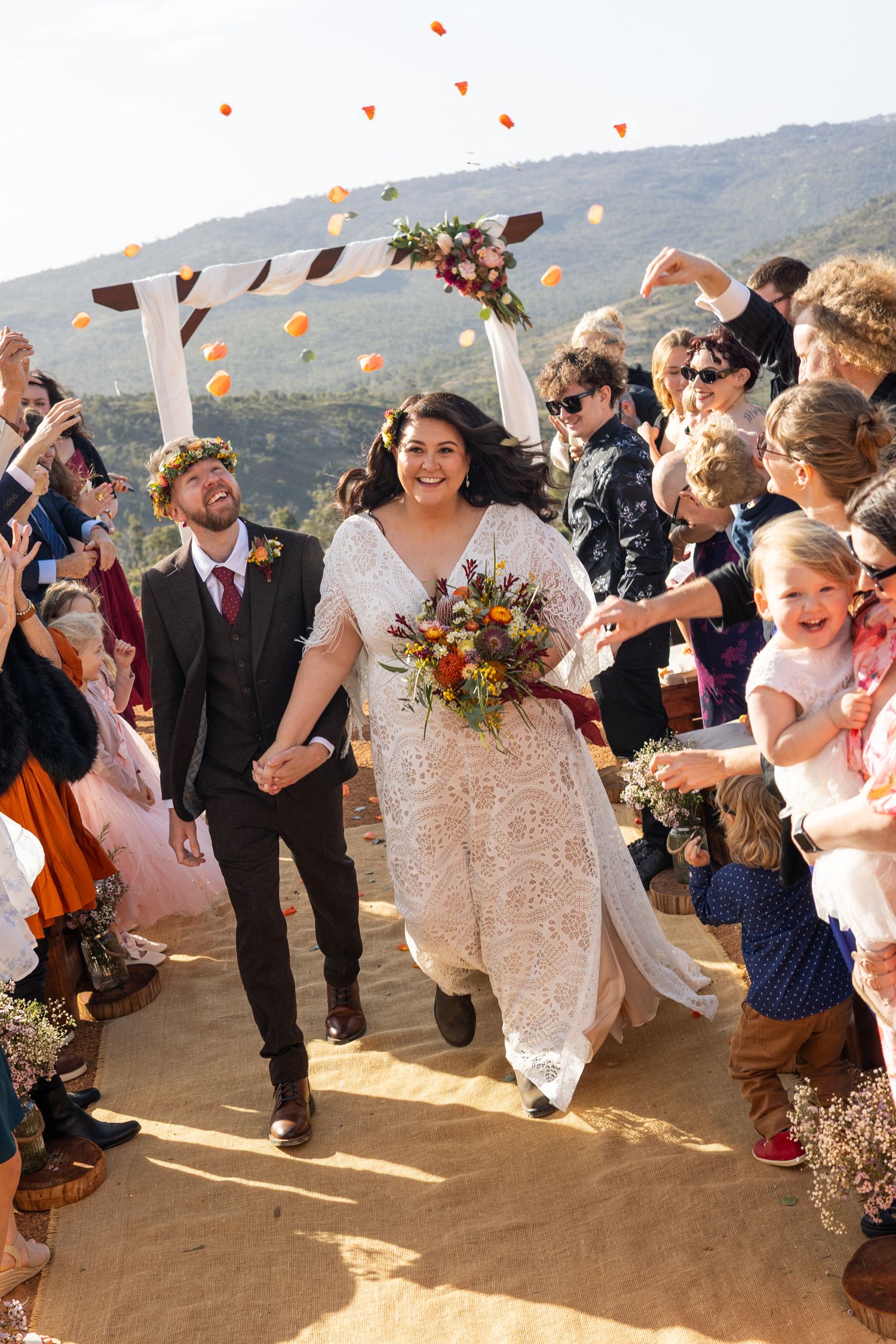 Wedding guests celebrate and dance joyfully on an outdoor deck with mountains visible in the background.