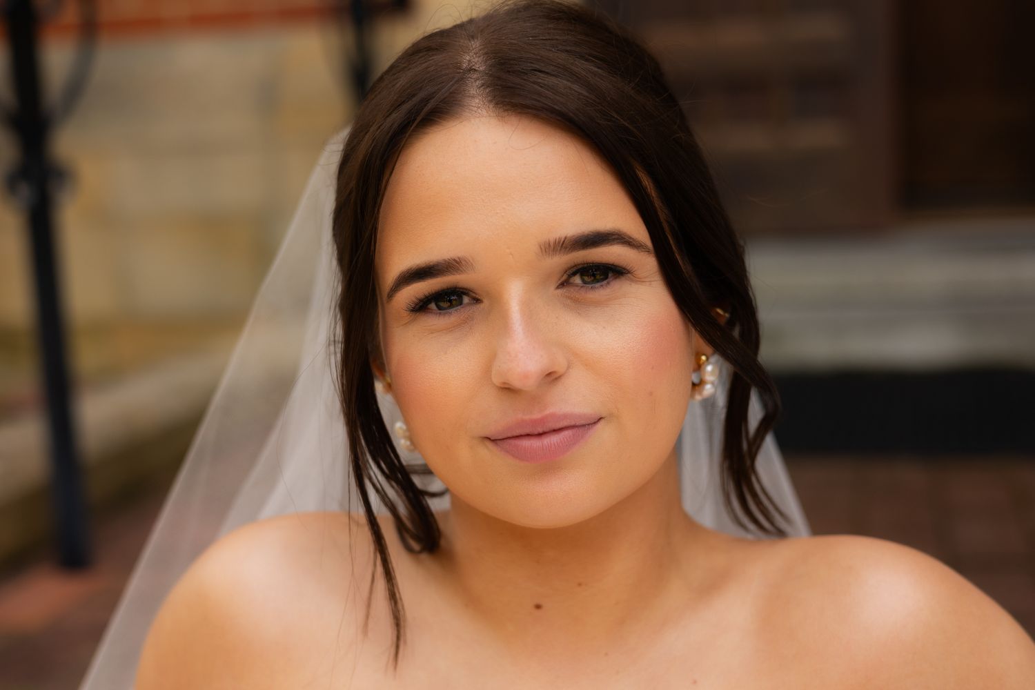 A bride in a white wedding dress poses with a soft smile in an elegant indoor setting.