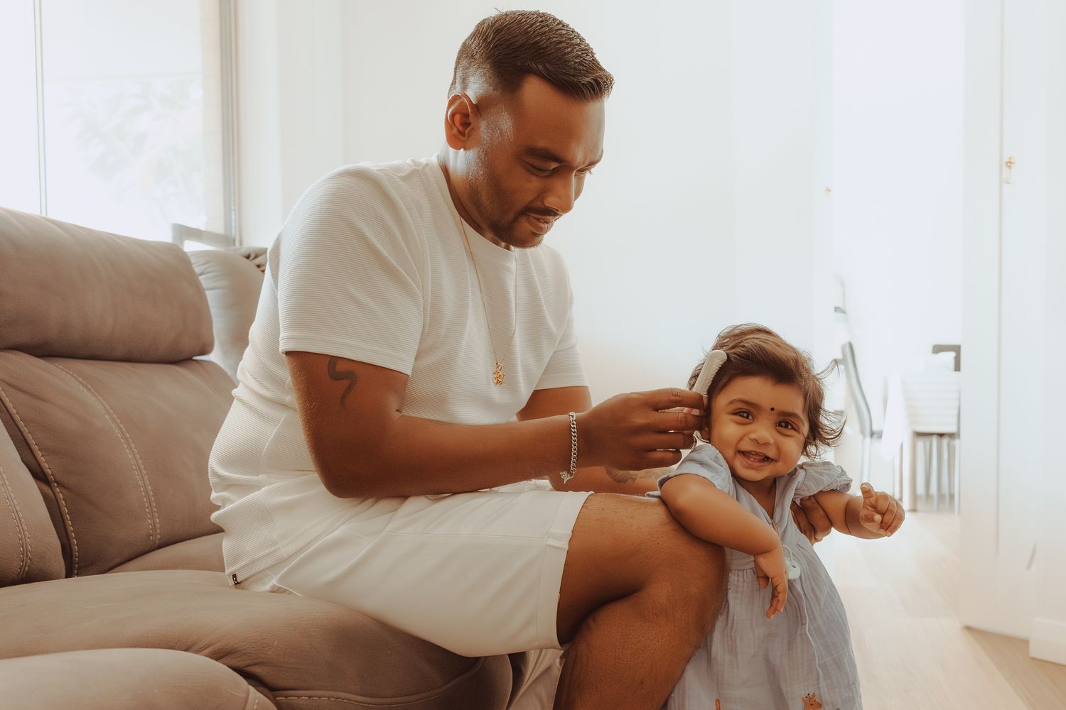 A parent and child share a tender moment while sitting together on a couch in a bright, modern living room.