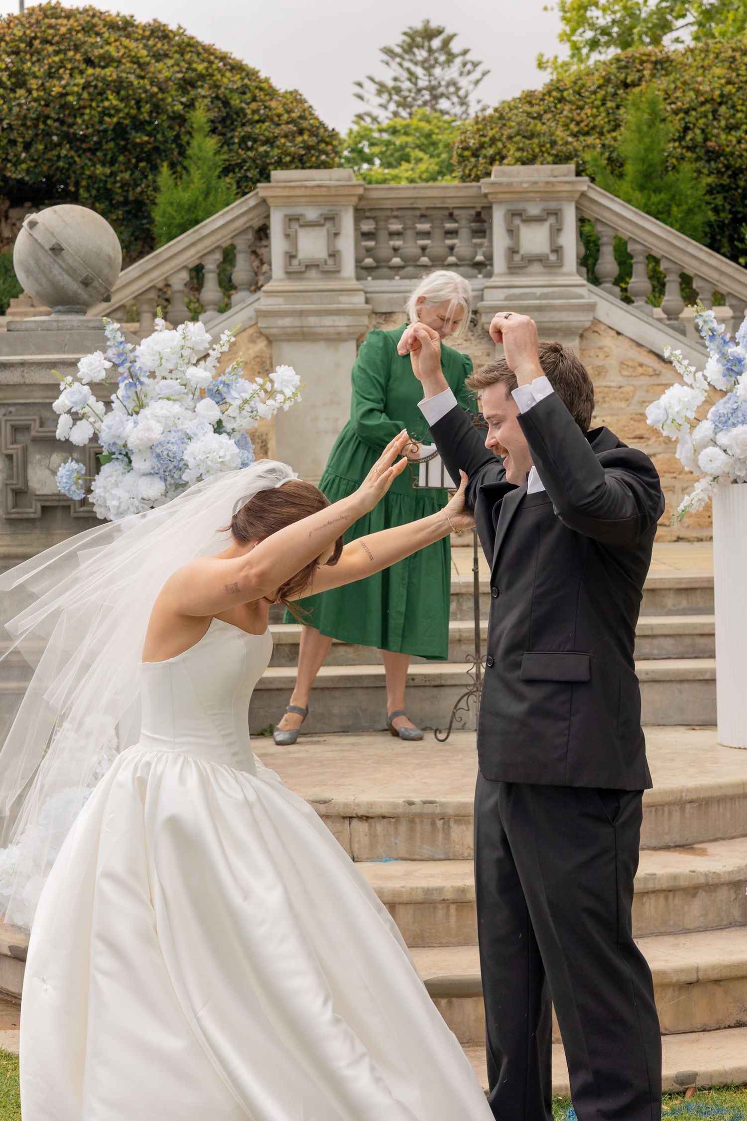 A playful wedding couple performs a fun action sequence across multiple frames on stone steps with blue hydrangeas.