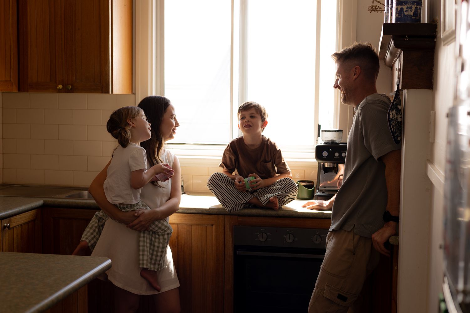 People gathered in a warm-lit kitchen having a casual conversation near wooden cabinets.