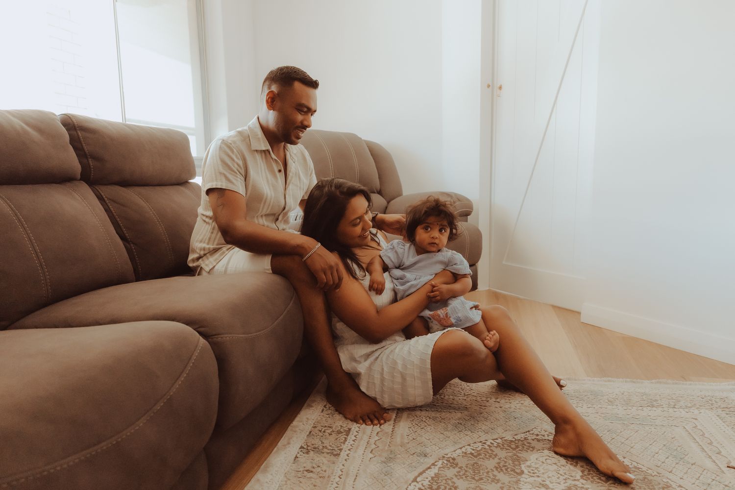 Parent and child sitting on couch looking at digital tablet together in bright living room.