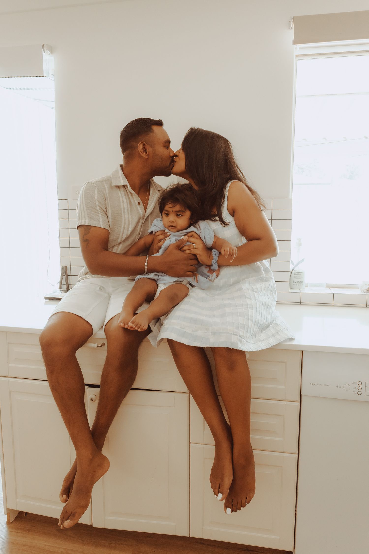 A family shares tender moments together in a bright white kitchen, sitting on countertops in a sequence of loving poses.