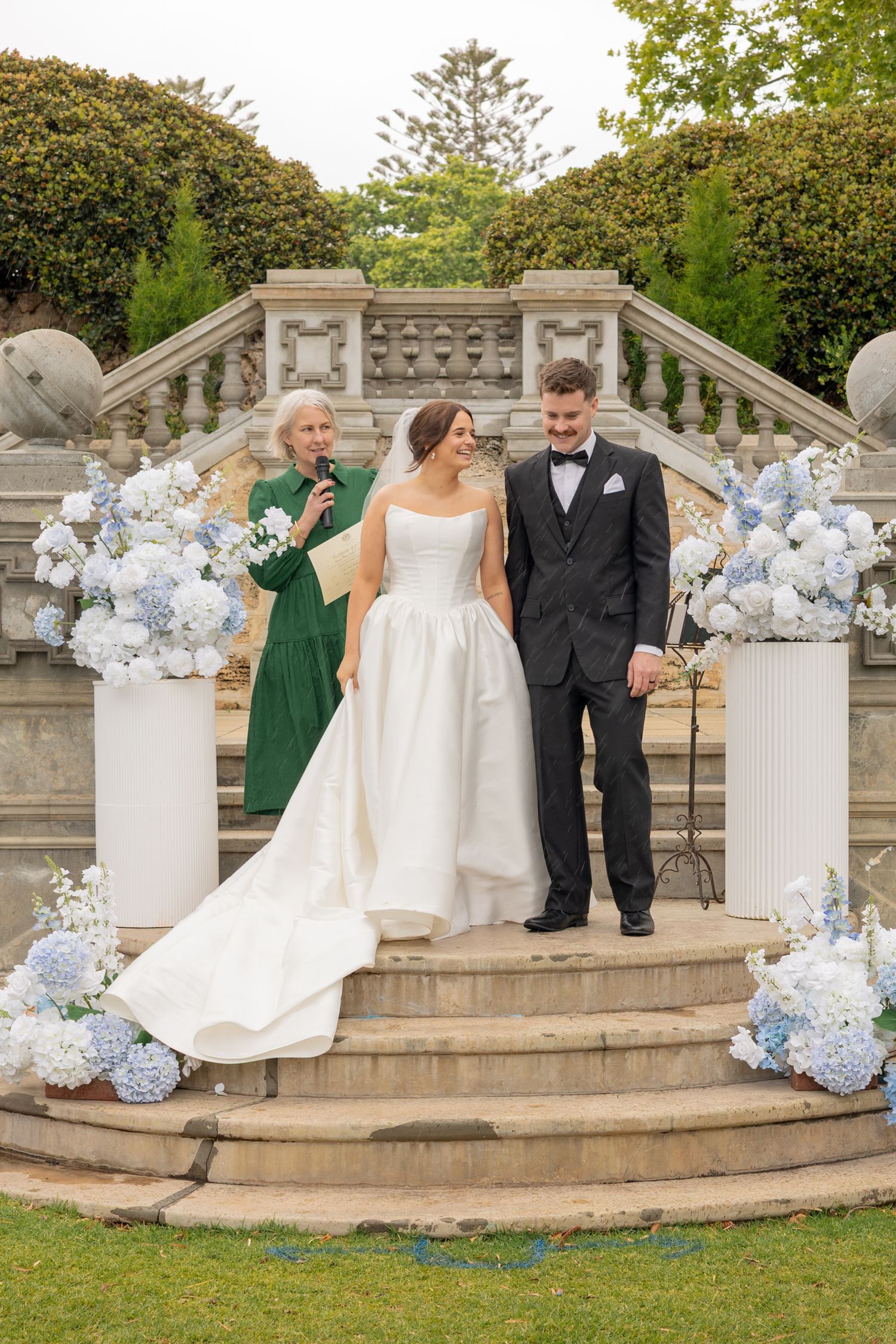 Elegant wedding party poses on stone terrace decorated with white and blue hydrangea floral arrangements.