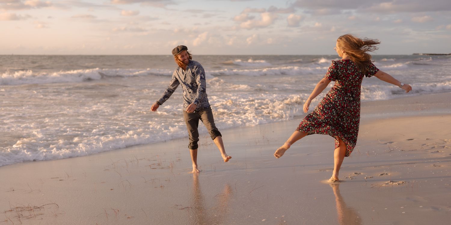 People playing and jumping on a sandy beach at sunset with ocean waves in the background.