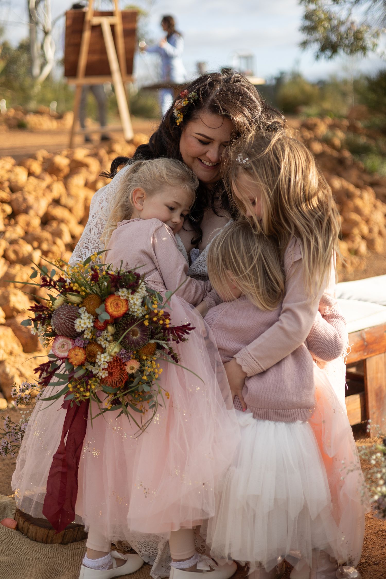 Young attendants in pink tulle dresses share a sweet embrace while holding autumn-colored bouquets outdoors. Perth wedding documentary photo