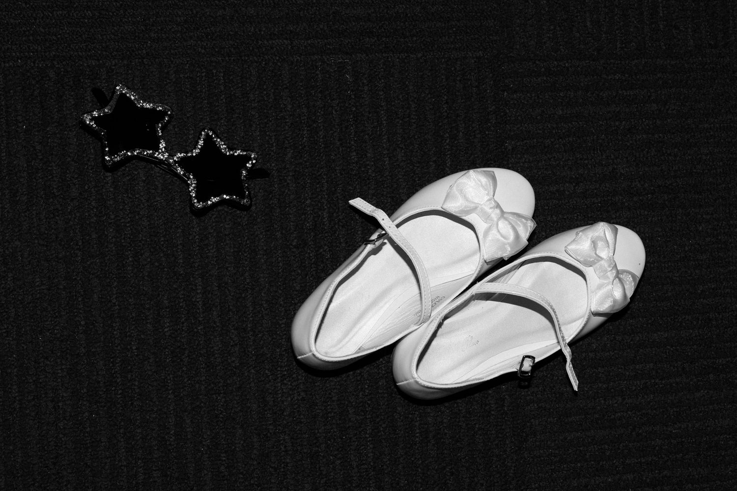 A pair of white ballet shoes on a black textured background with a decorative star shape in the corner.