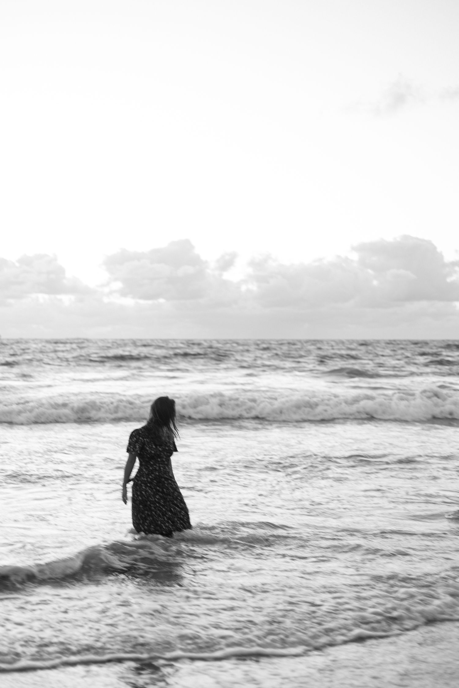 A black and white photo of a person in a dress standing in ocean waves. Perth Fremantle Photography