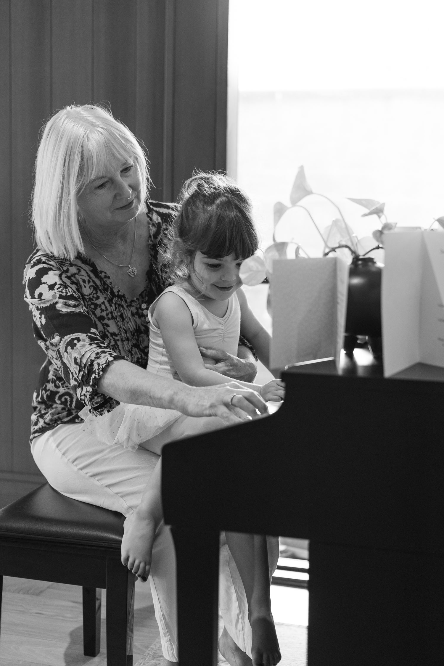 A heartwarming black and white photo showing piano practice time with shopping bags visible in the background.