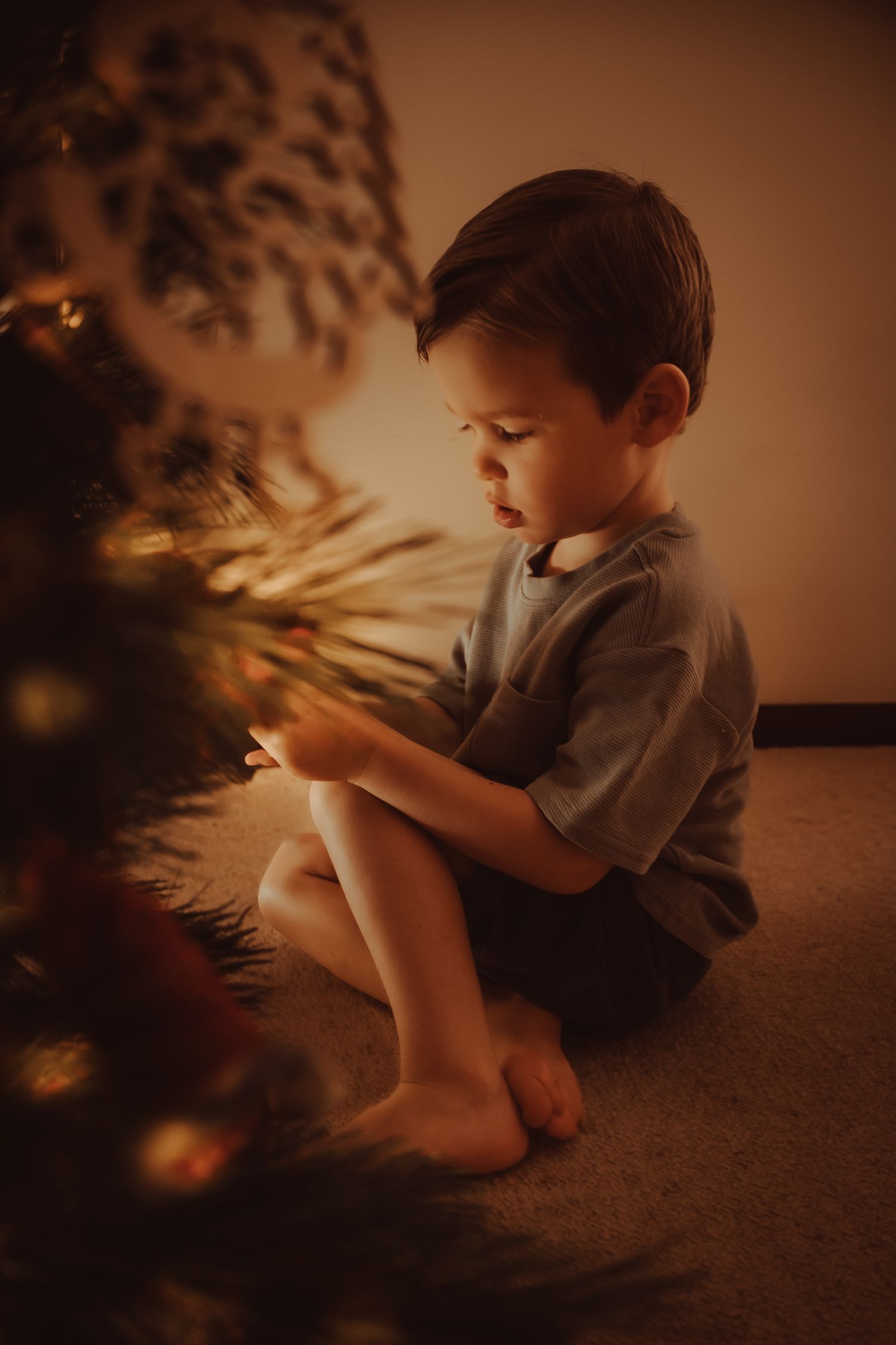A young child sits on a carpeted floor in warm lighting while playing with shadows and light.
