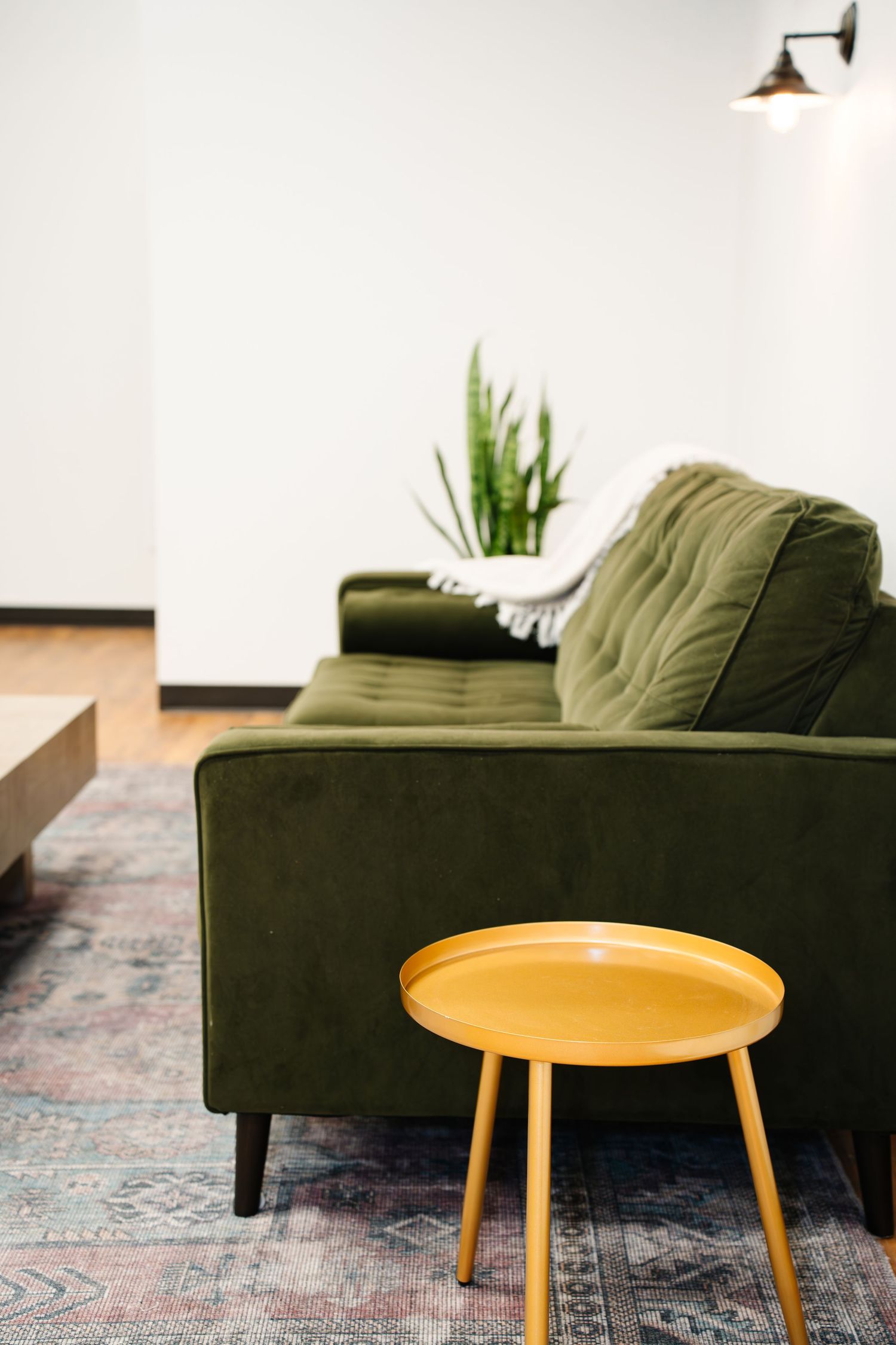 Modern living room interior with dark green velvet sofa and yellow side table on patterned area rug for gatherings.