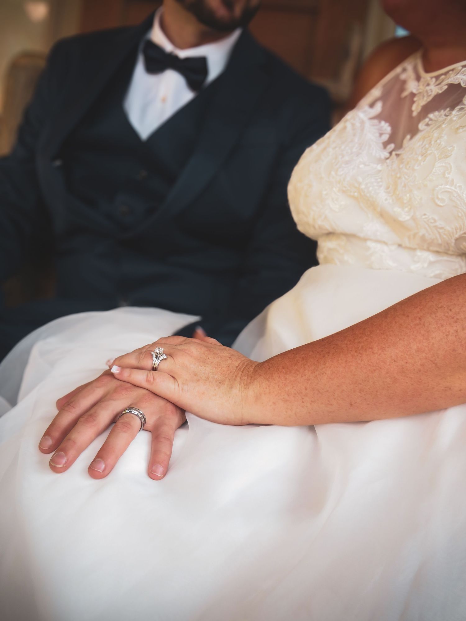 Close-up of wedding rings and hands resting on white dress fabric.
