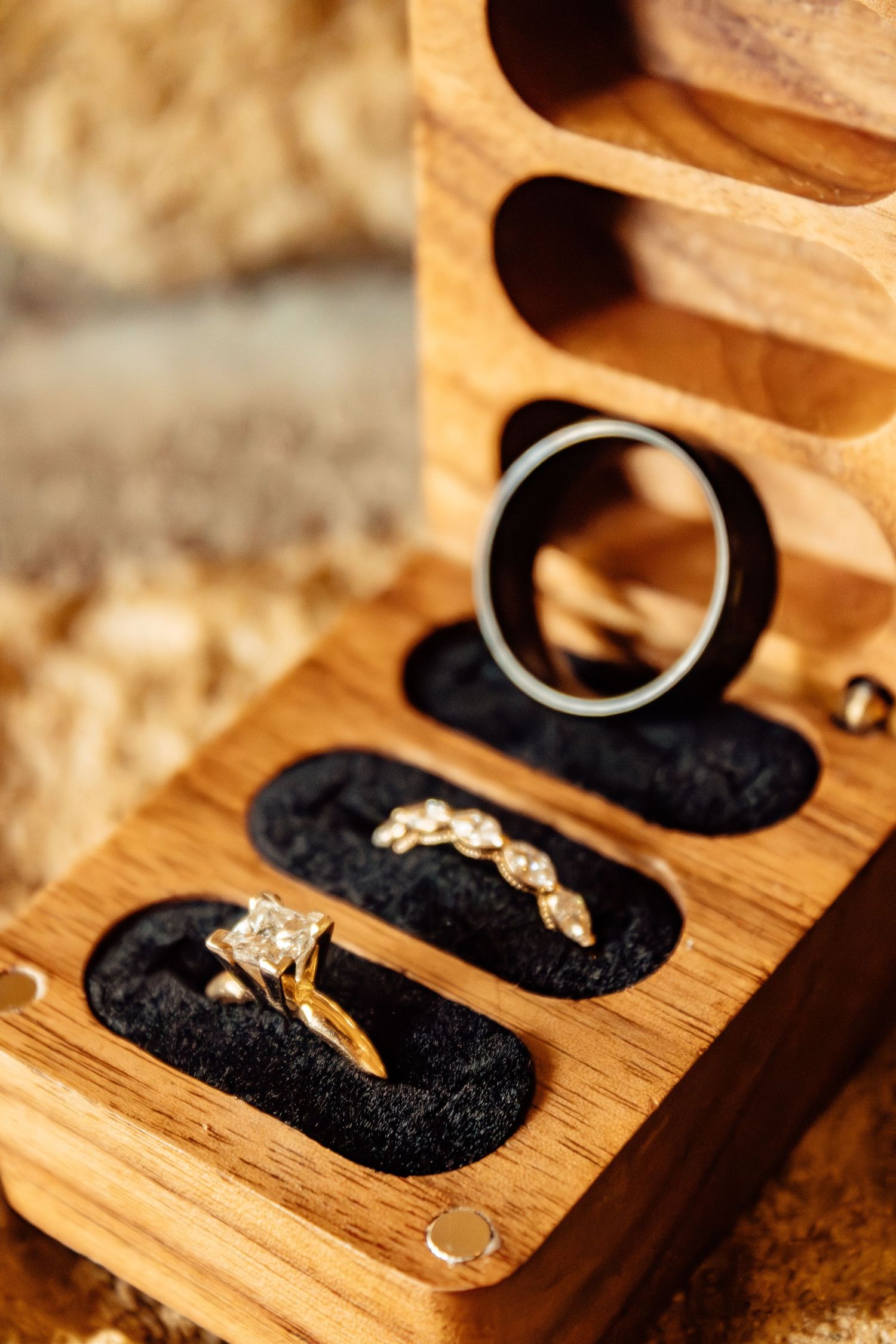 Close-up of engagement rings nestled in a wooden presentation box with black velvet interior.