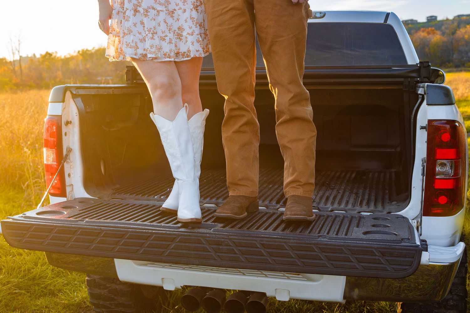 Boots and casual attire visible near white pickup truck tailgate at sunset.