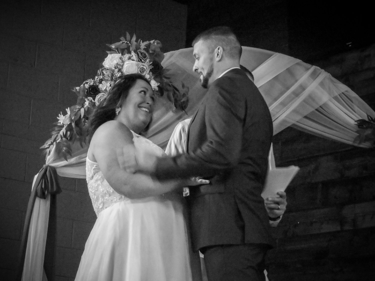 Black and white photo of emotional wedding ceremony moment under floral arch.