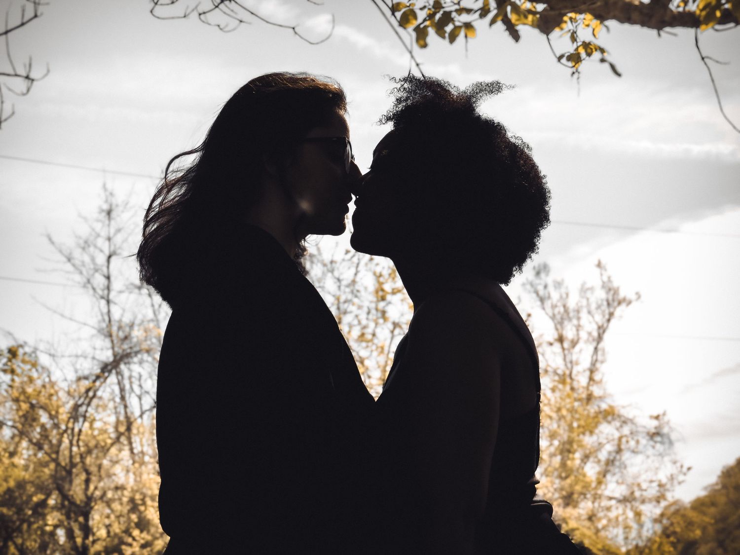 Silhouette of couple sharing intimate moment against bright sky.