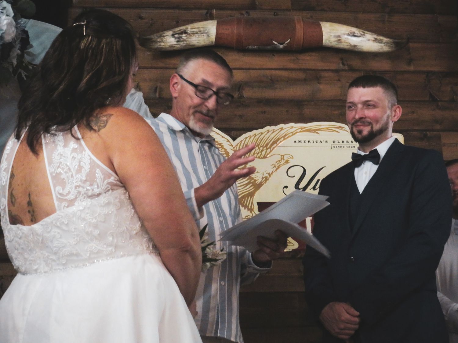 Wedding ceremony in rustic wooden venue with officiant reading from ceremony script.