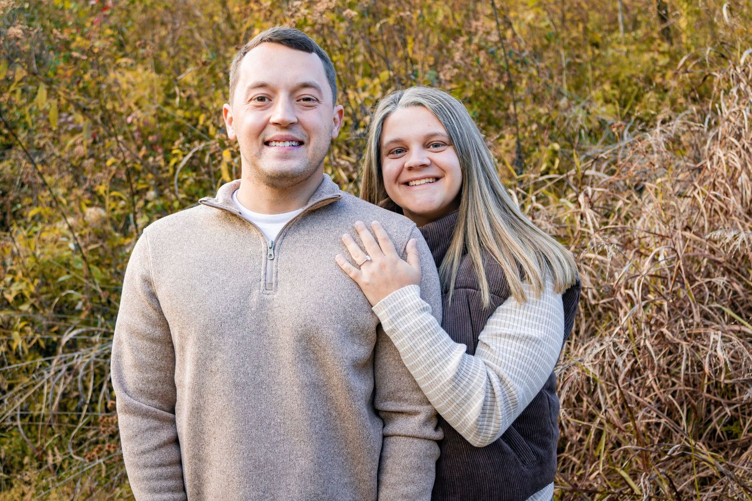 Couple embracing outdoors during autumn photoshoot wearing neutral sweaters.