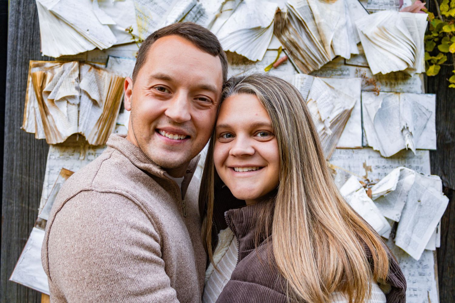 Happy couple posing against wall covered in scattered papers.