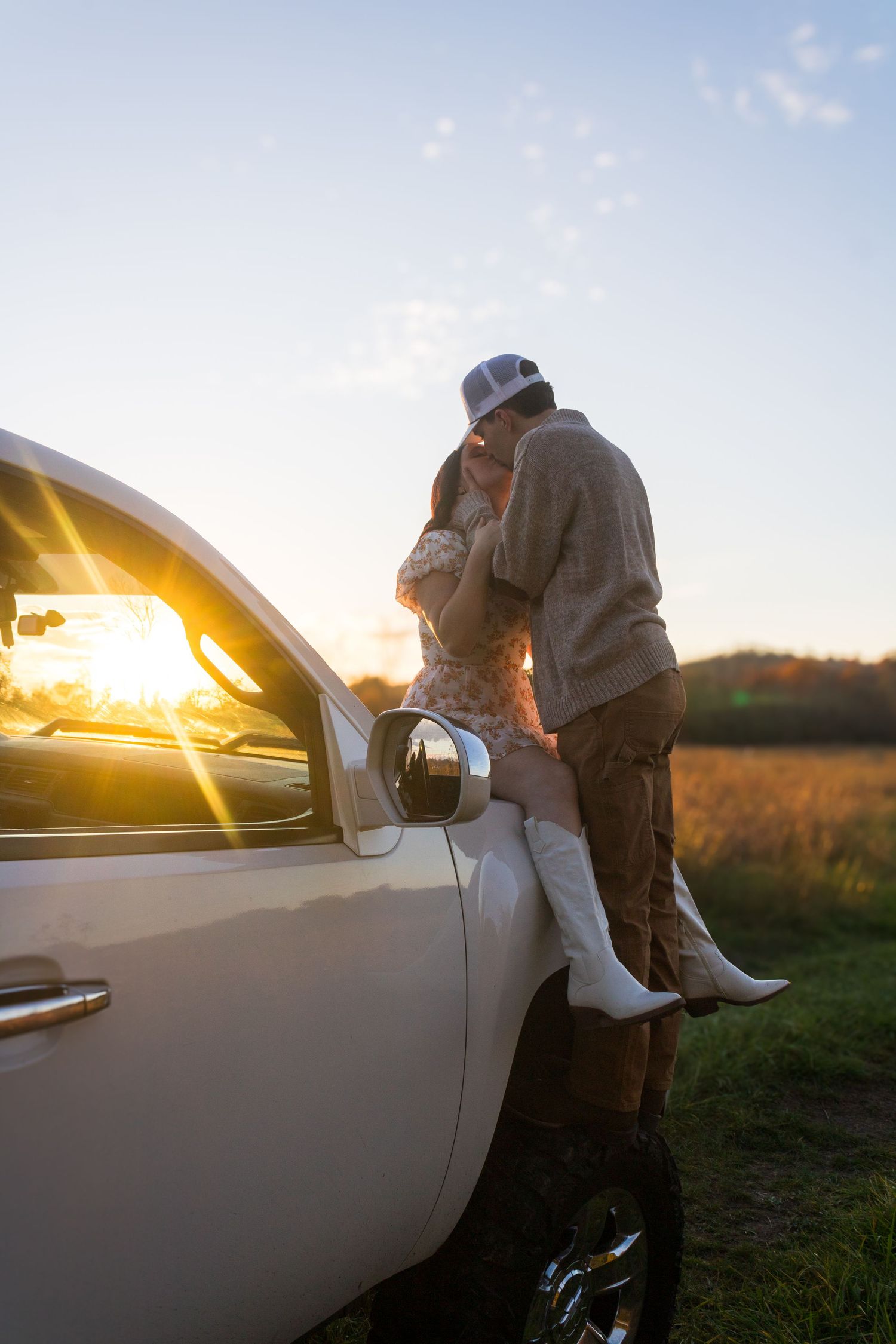 Silhouetted figures share tender moment against sunset by white truck.