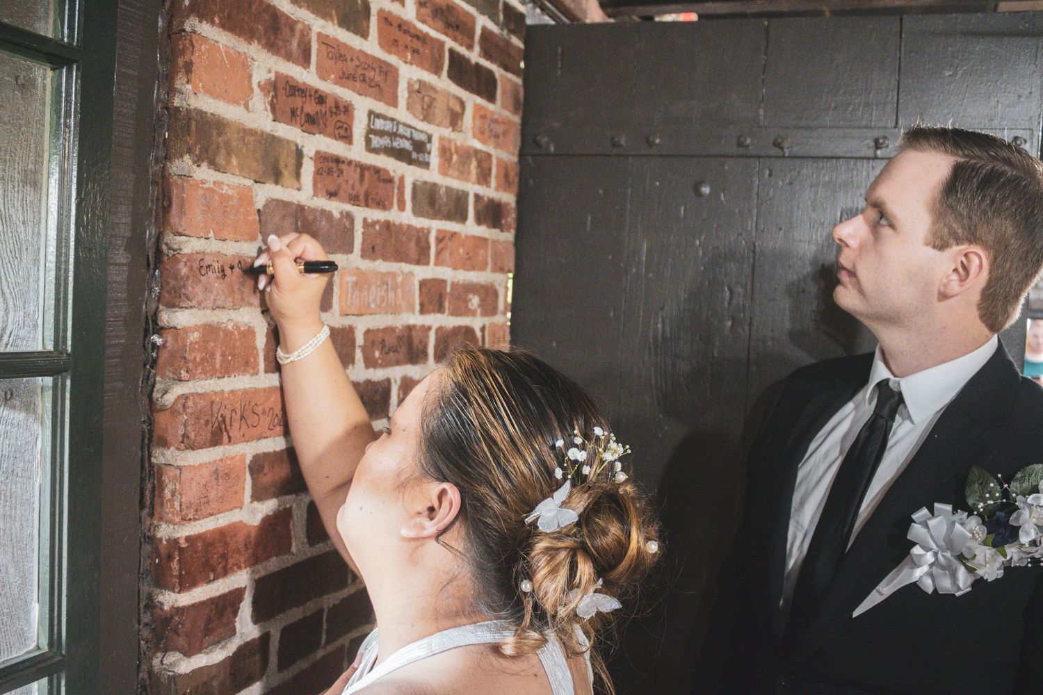 A couple signs their names on a brick wall during their wedding celebration.