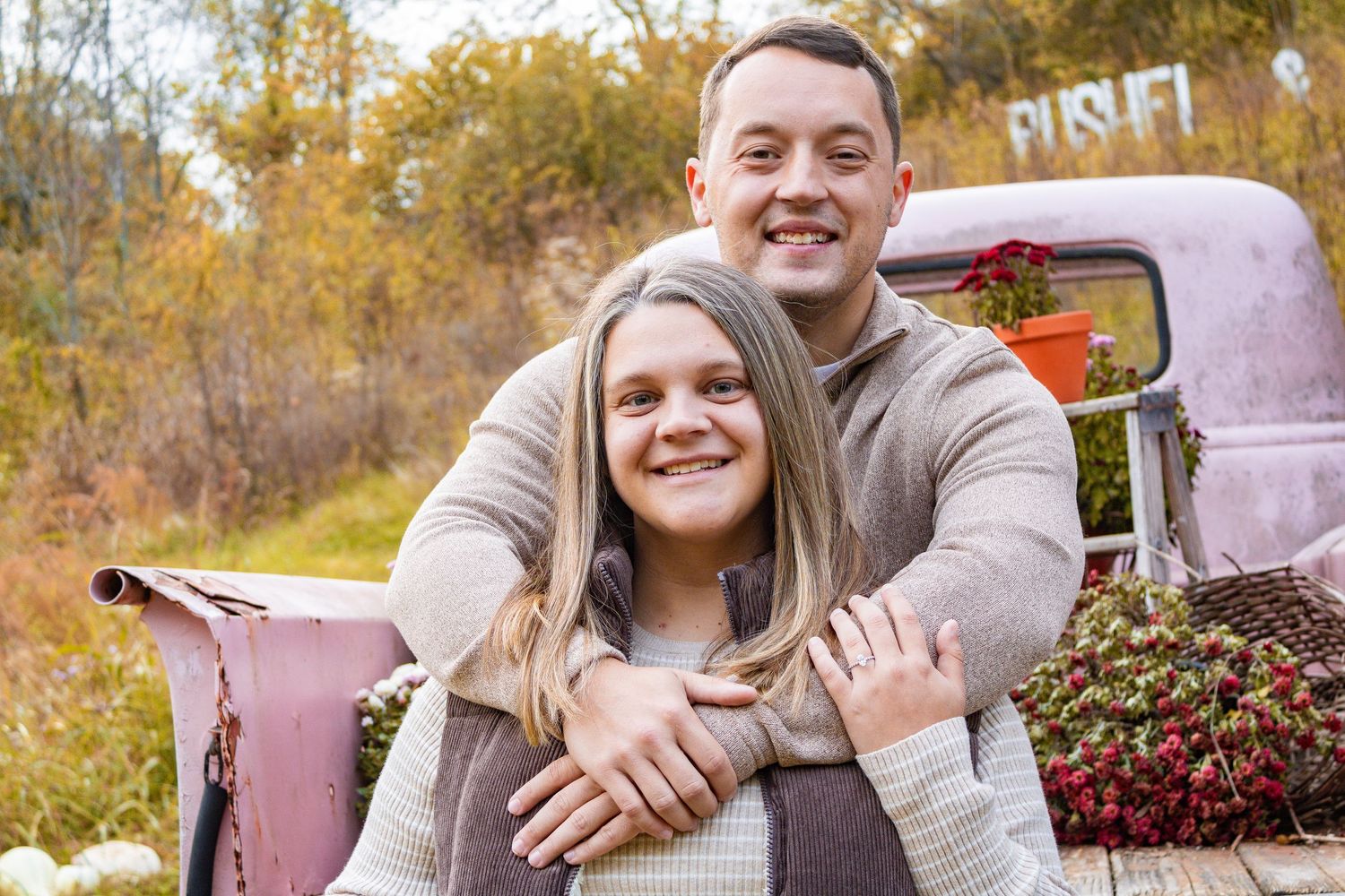 Couple poses together in front of vintage pink truck during autumn season.