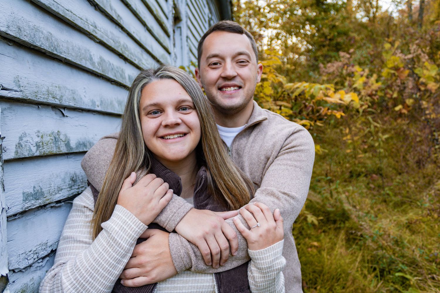 Happy couple embracing against rustic wall during fall photoshoot.