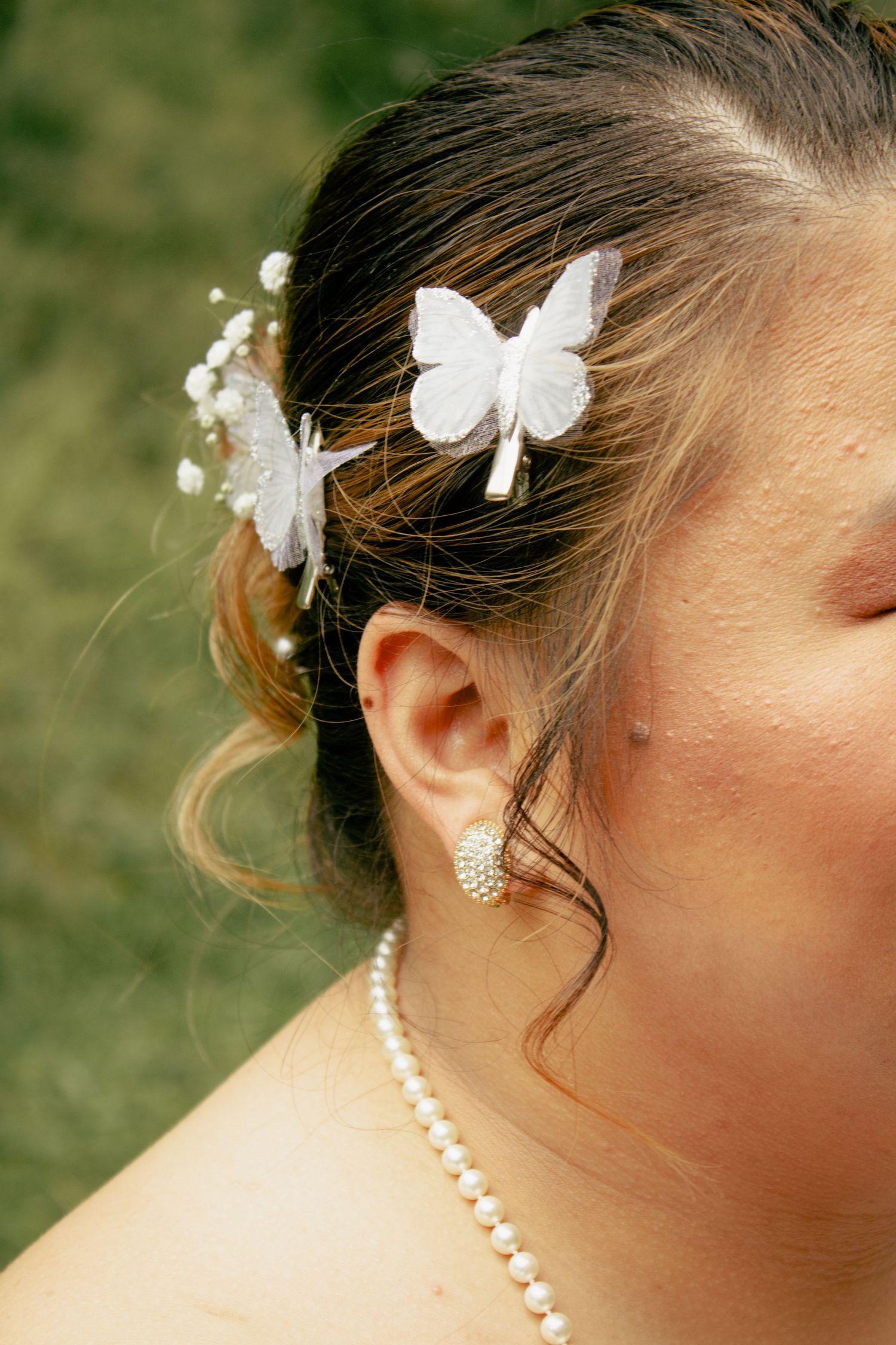 Close-up of delicate white butterfly hair accessories and pearl jewelry worn by a bride.