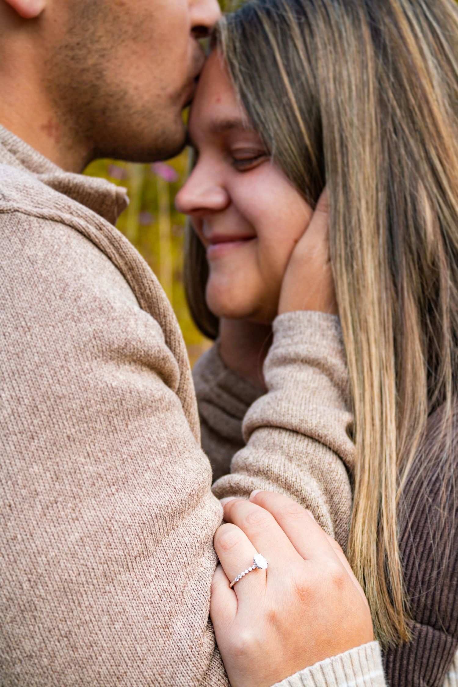 Intimate moment between couple wearing neutral sweaters during engagement photoshoot.