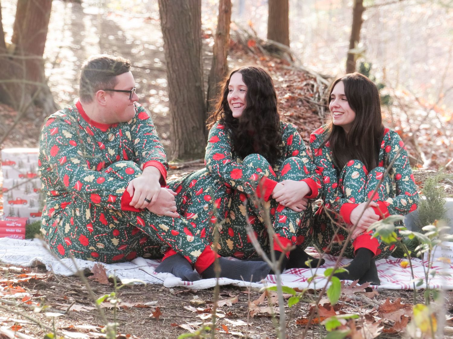 Family wearing matching Christmas pajamas having fun on picnic blanket in woods.