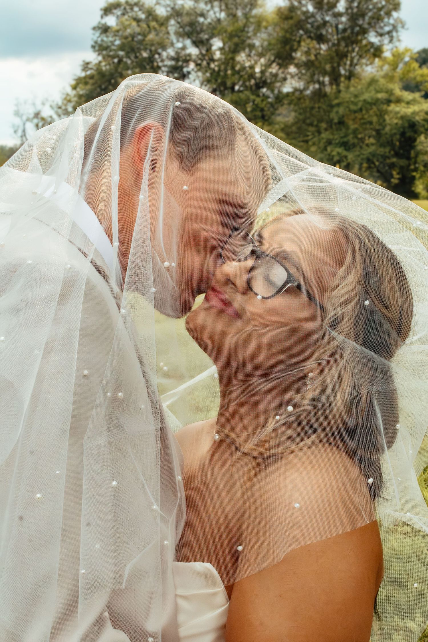 A romantic wedding moment captured through a delicate veil in an outdoor garden setting.