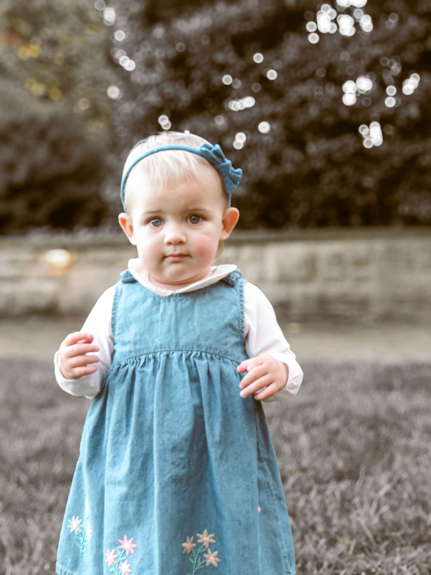 Small child wearing a blue embroidered dress and matching headband stands outdoors.