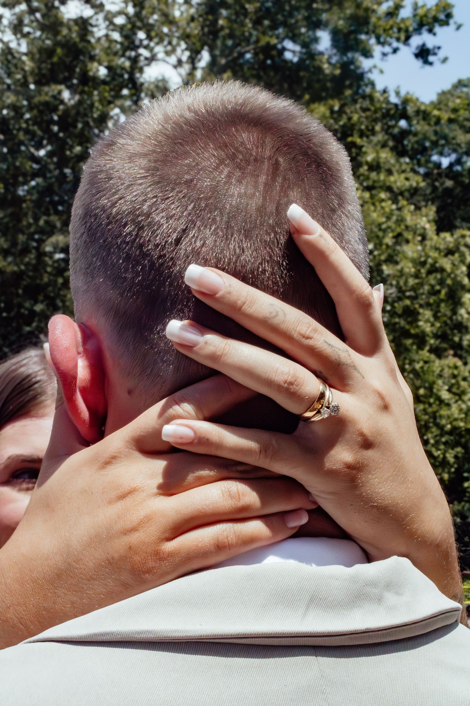 Close-up of hands with wedding rings embracing against an outdoor background.