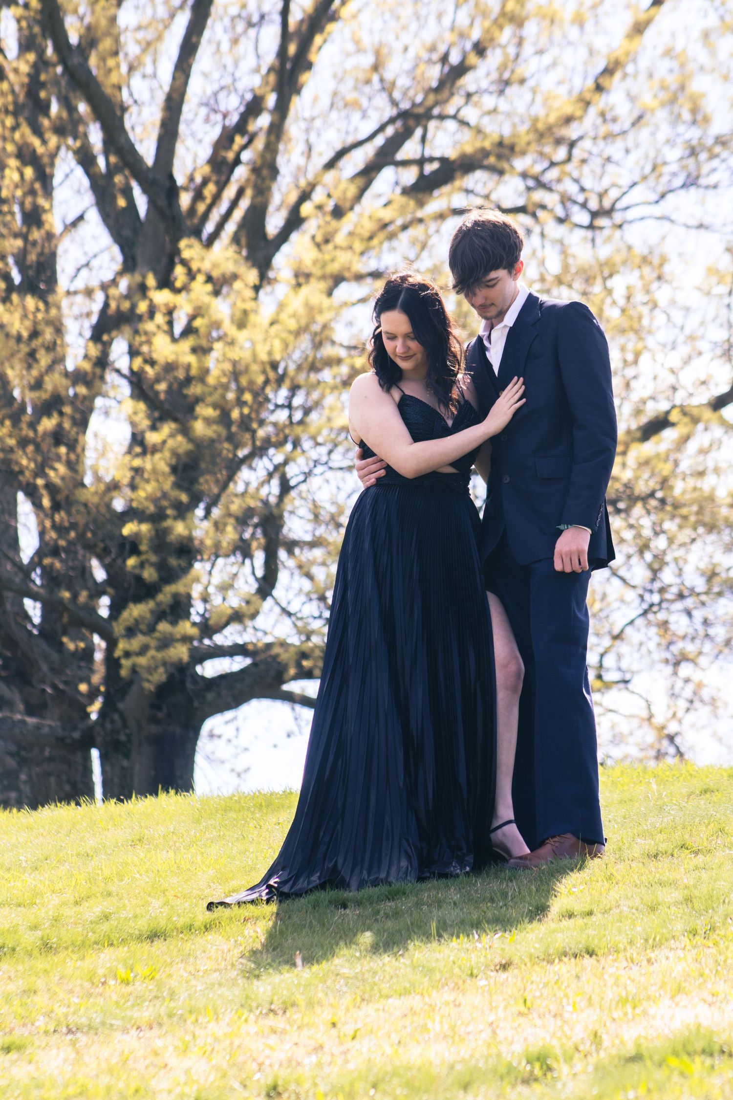 Couple in formal attire posing together on a sunny hillside.
