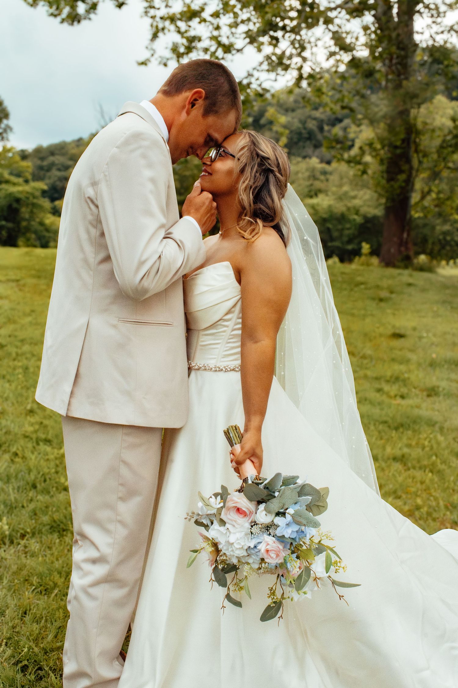 Bride and groom share intimate moments in white wedding attire while holding a blue and white bouquet.