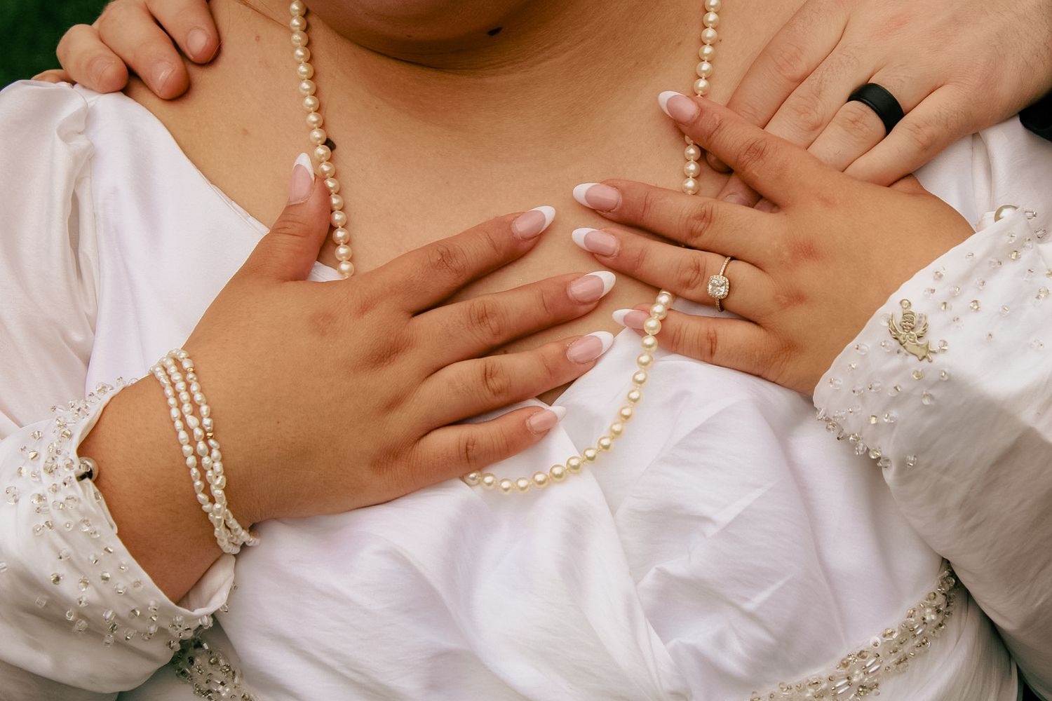 Close-up of hands wearing wedding rings with pearl necklace details.
