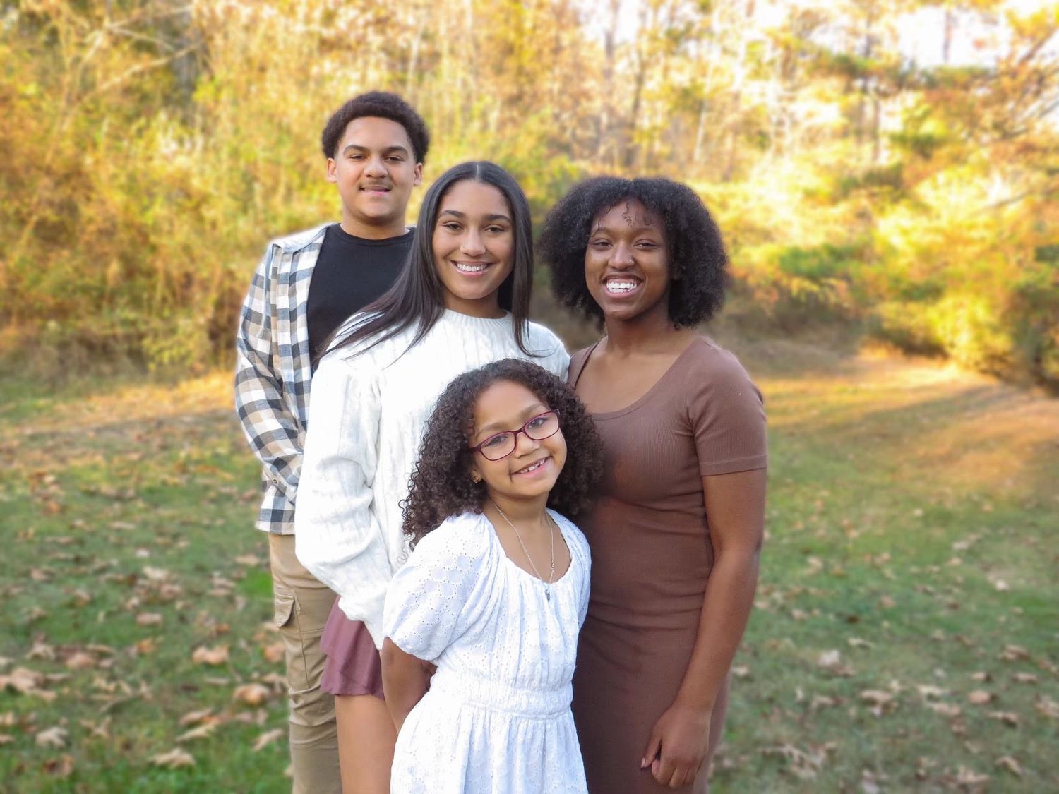 A group poses together outdoors in autumn with warm sunlight filtering through trees in the background.