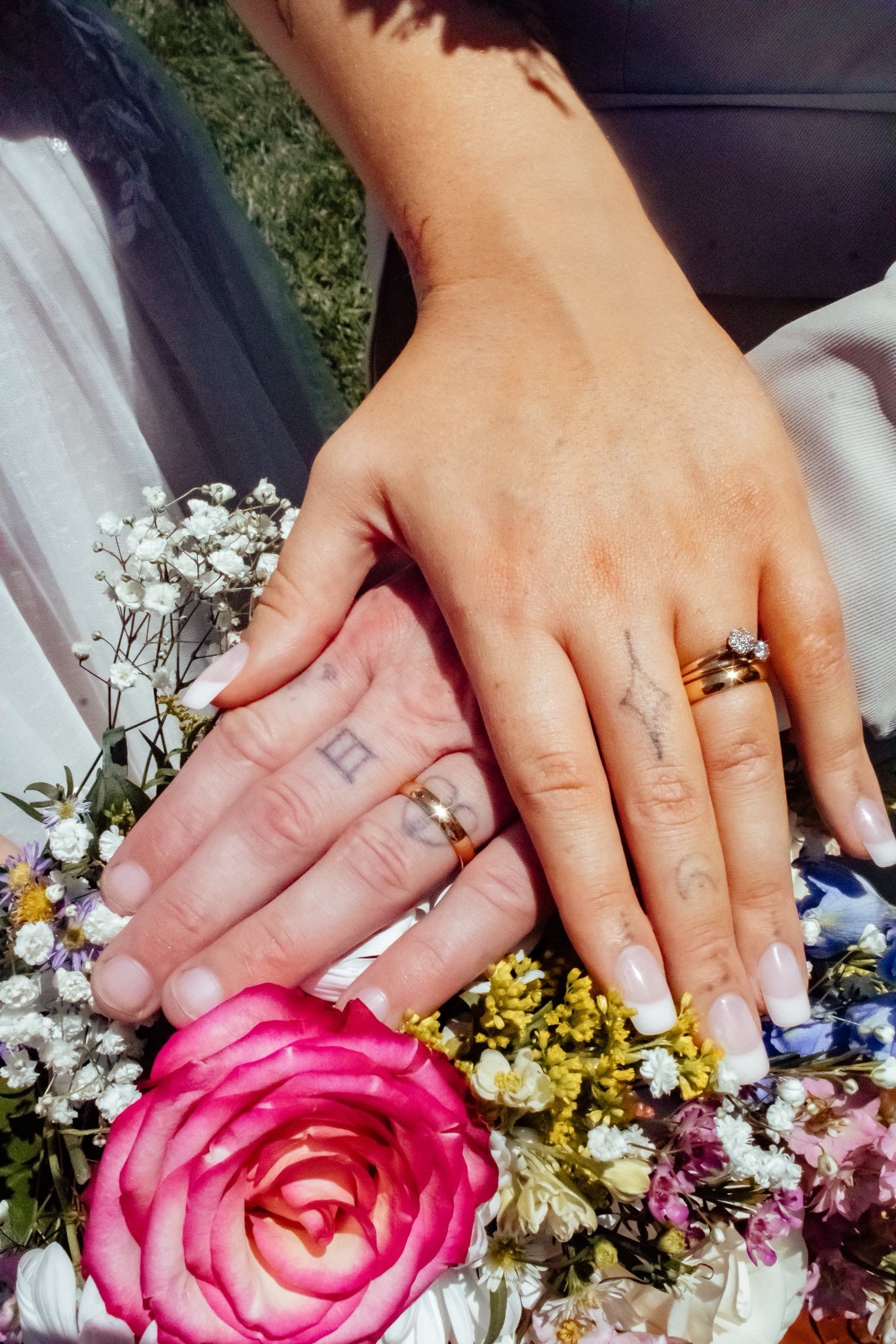Close-up of hands displaying engagement rings among delicate pink roses and white baby's breath flowers.