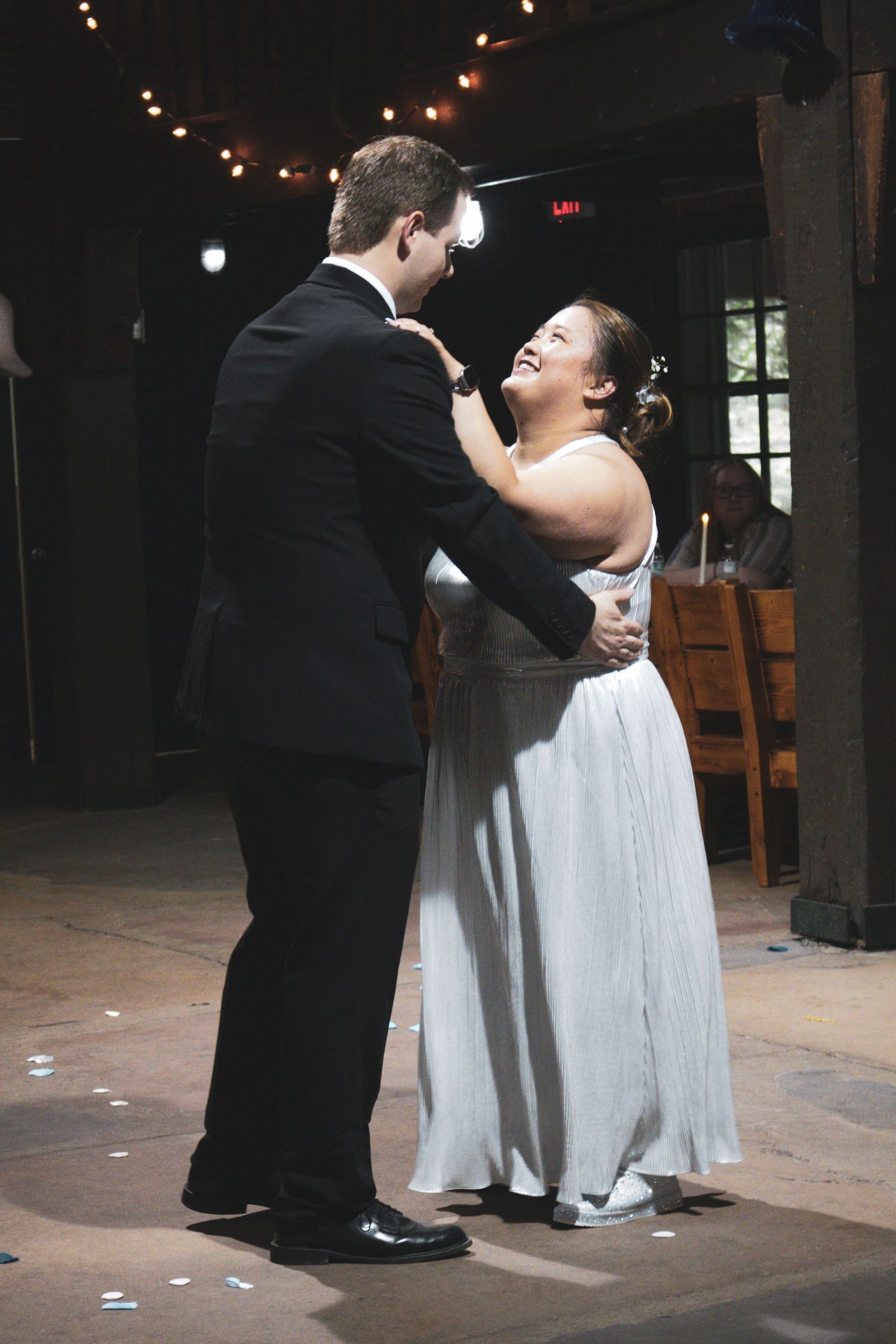 A romantic first dance between newlyweds under string lights at their wedding reception.