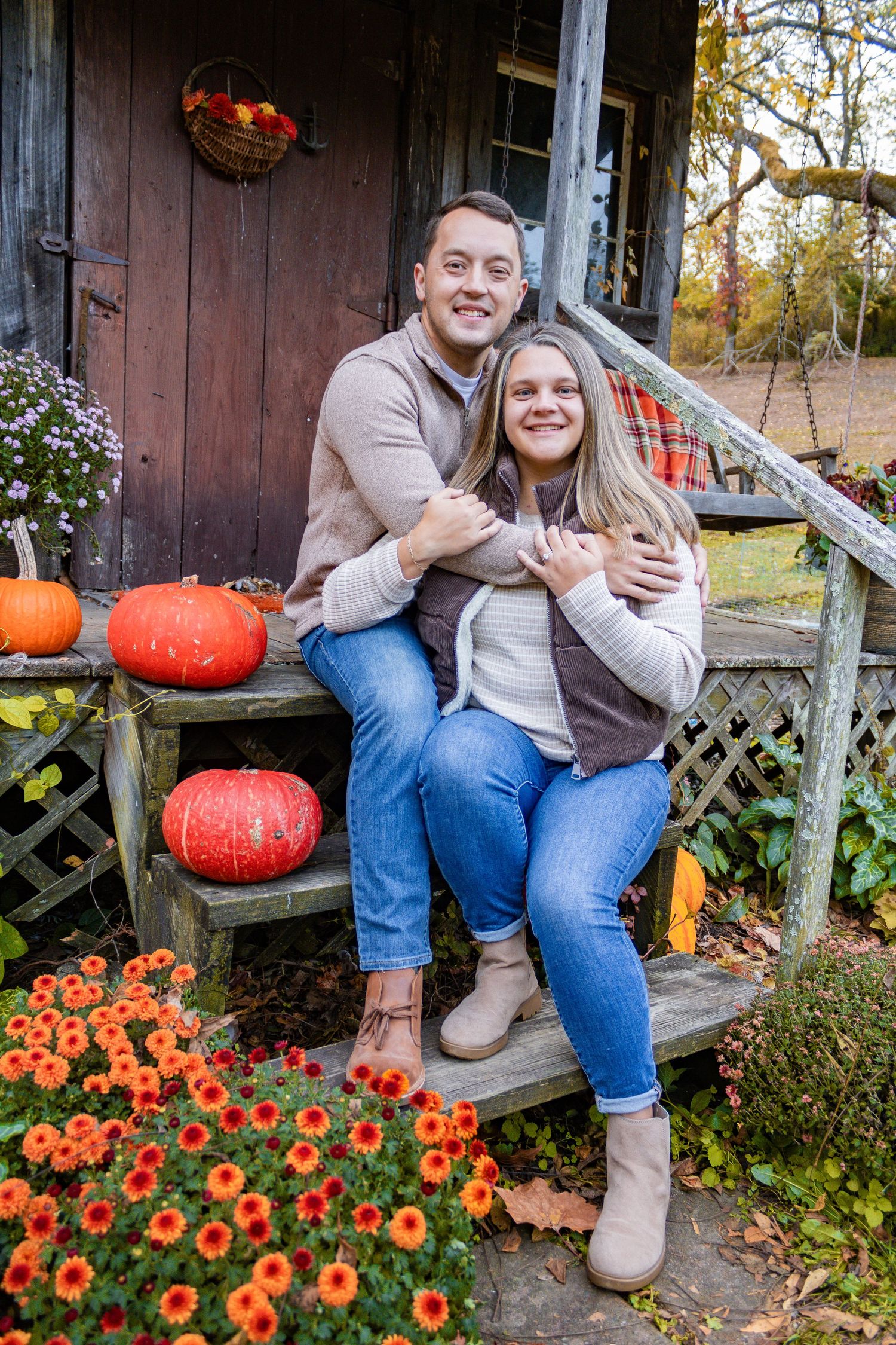 Couple sitting on rustic porch steps decorated with pumpkins and orange flowers.