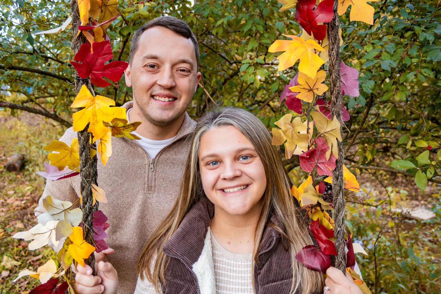 Couple smiling among colorful autumn leaves and foliage.