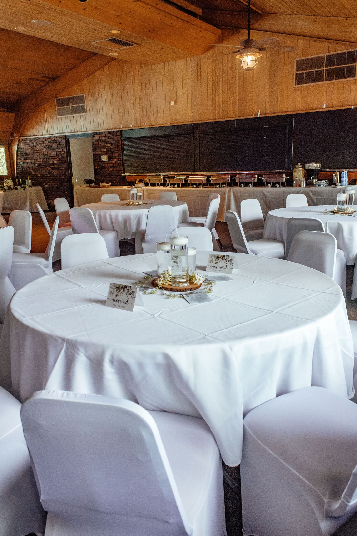 Wedding reception venue with white-clothed round tables and wooden ceiling details.