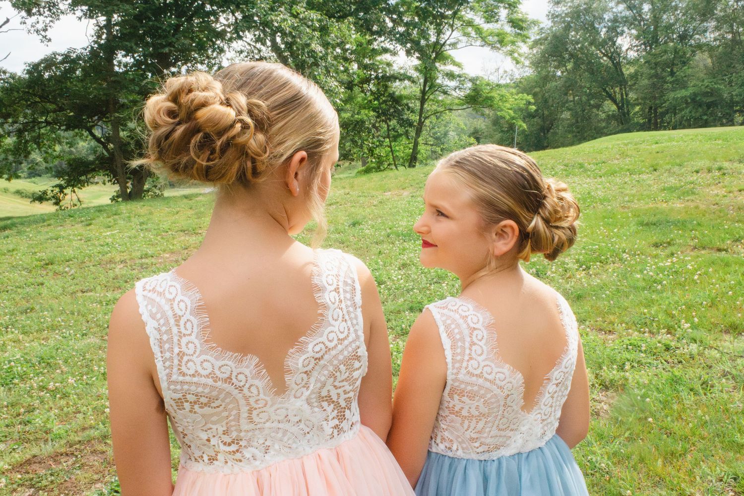 Bridesmaids in matching lace dresses photographed from behind in an outdoor setting.