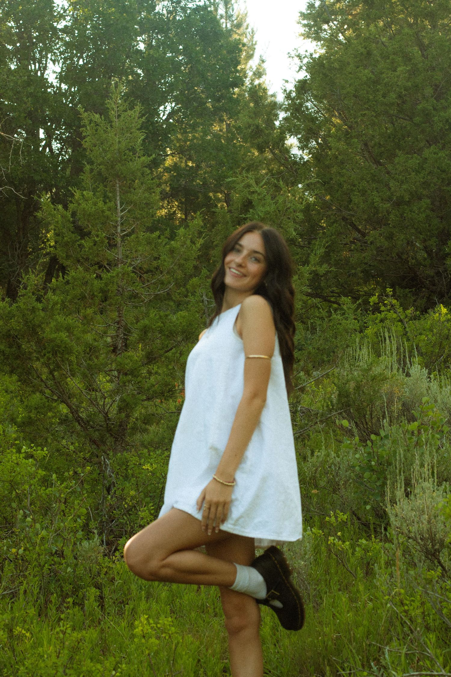 Person in white top posing playfully in a wildflower meadow during golden hour.