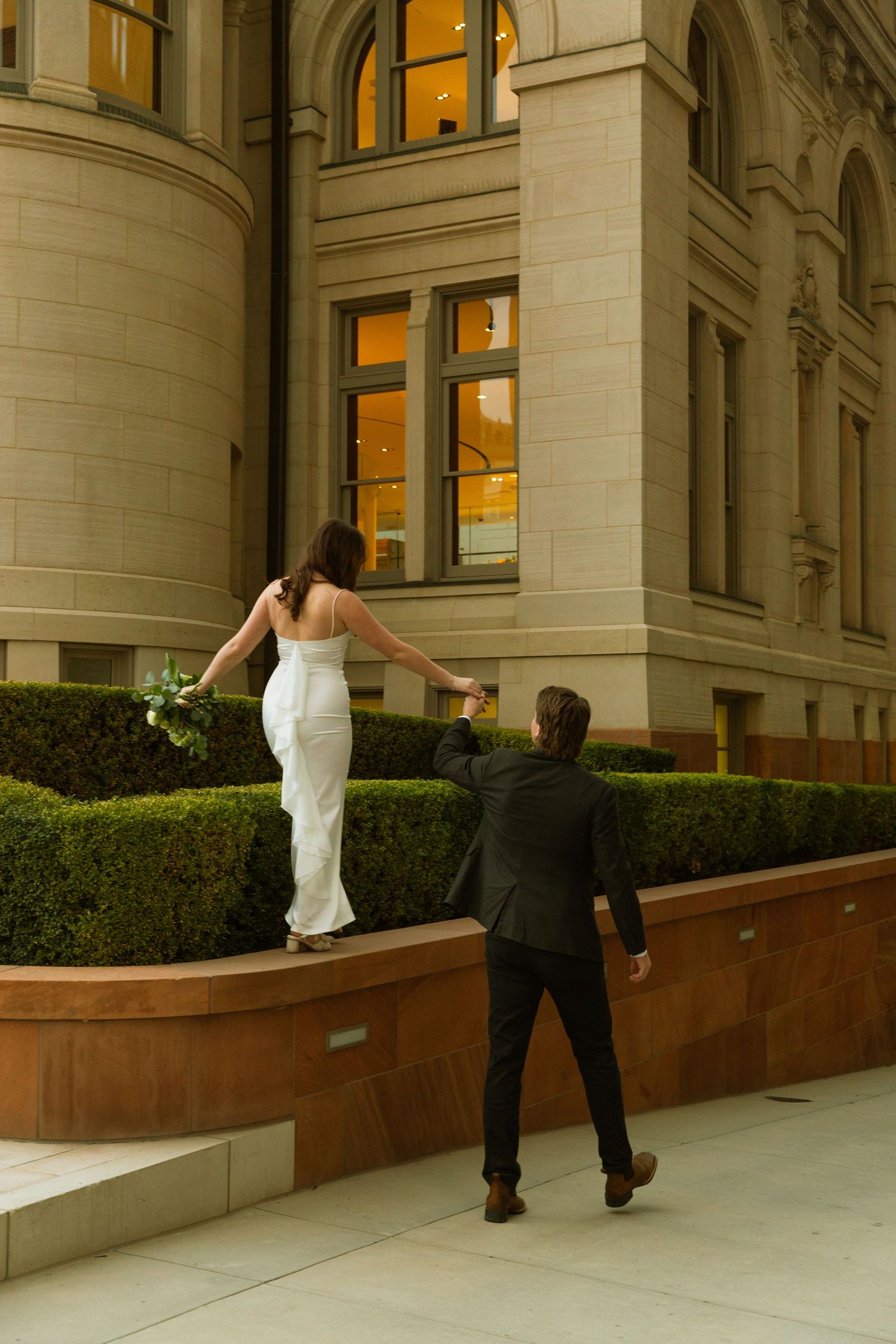 A sequence of four photos showing a bride and groom walking along a building's exterior wall.
